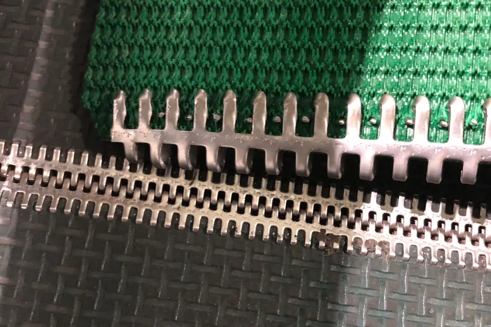 Detail sambungan mekanis pada tepi belt conveyor PVC hijau, dua baris pelat kawat gigi terpasang rapat dan saling mengunci